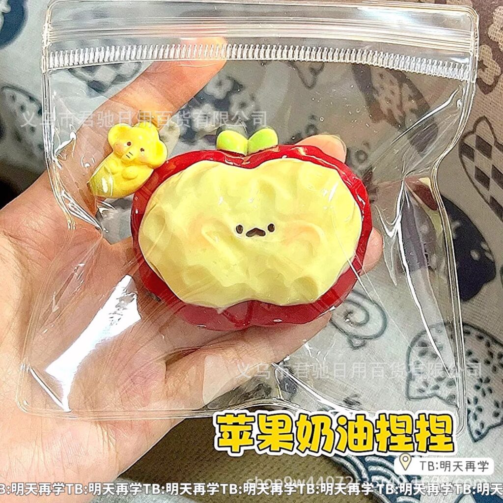 Creamy red apple squishy with a yellow center, green leaf and cute face in a clear pouch