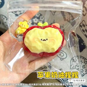 Creamy red apple squishy with a yellow center, green leaf and cute face in a clear pouch